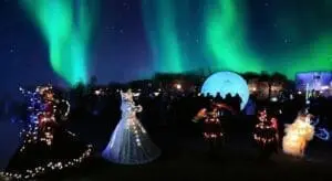 The picture shows a dance show in Celle. The show is in the evening. The dancers wear glowing dresses. Green northern lights are in the sky. Many people watch the show. It is a special experience.