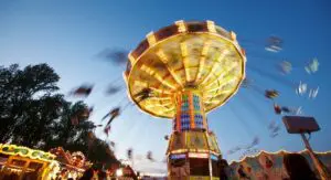 Das Bild zeigt das Schützenfest in Hannover. Ein großes, buntes Karussell dreht sich schnell. Es ist Abend und überall sind Lichter.