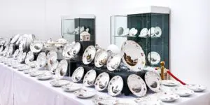 Bilden visar konstnärligt målade porslinstallrikar. Tallrikarna står på ett vitt bord. Det finns färgglada bilder på tallrikarna. Tallrikarna är en del av en utställning på residensmuseet i Wolfenbüttel.